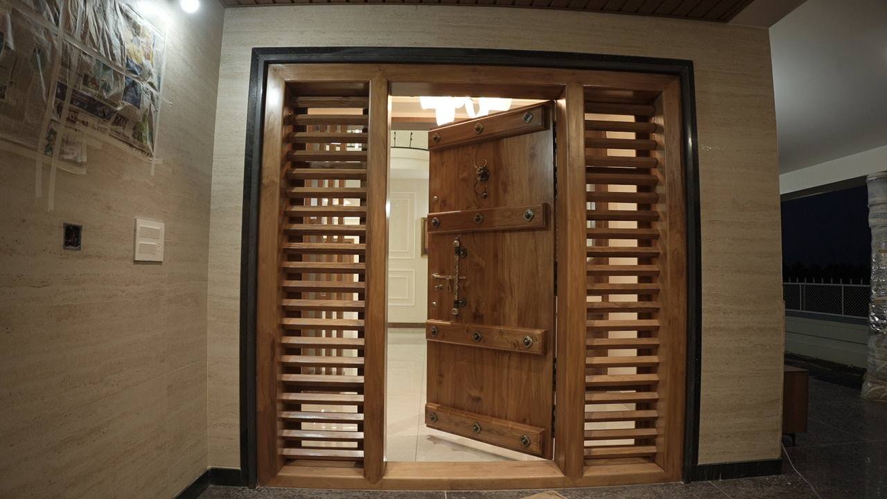 Carved teak main door swinging open between timber-slatted side panels